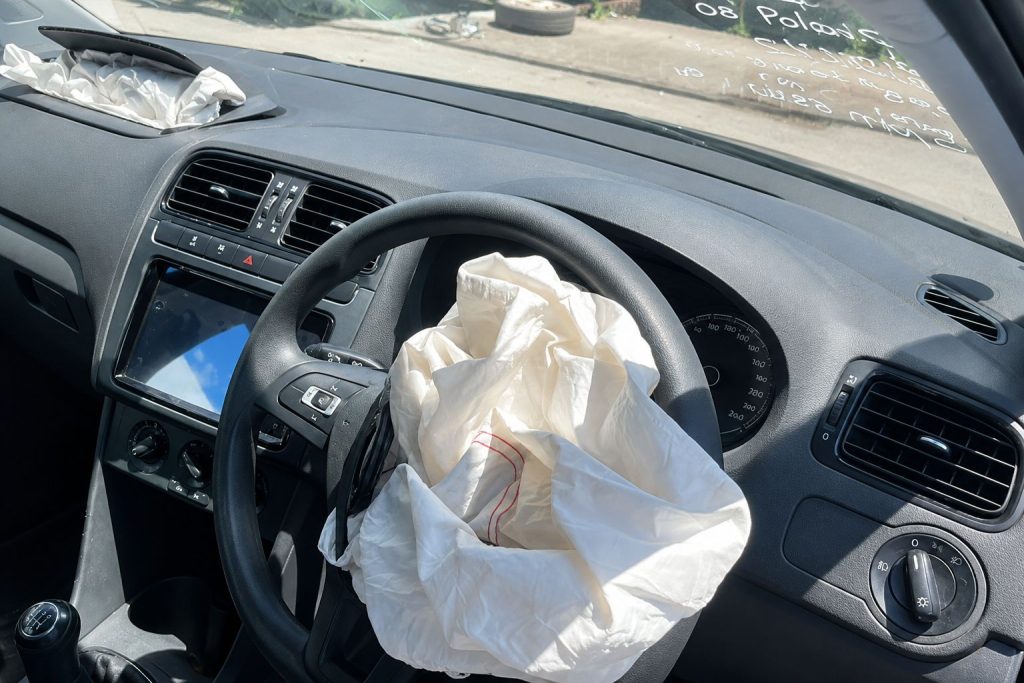 Deployed airbag in a vehicle interior after impact, showing steering wheel, dashboard, and controls